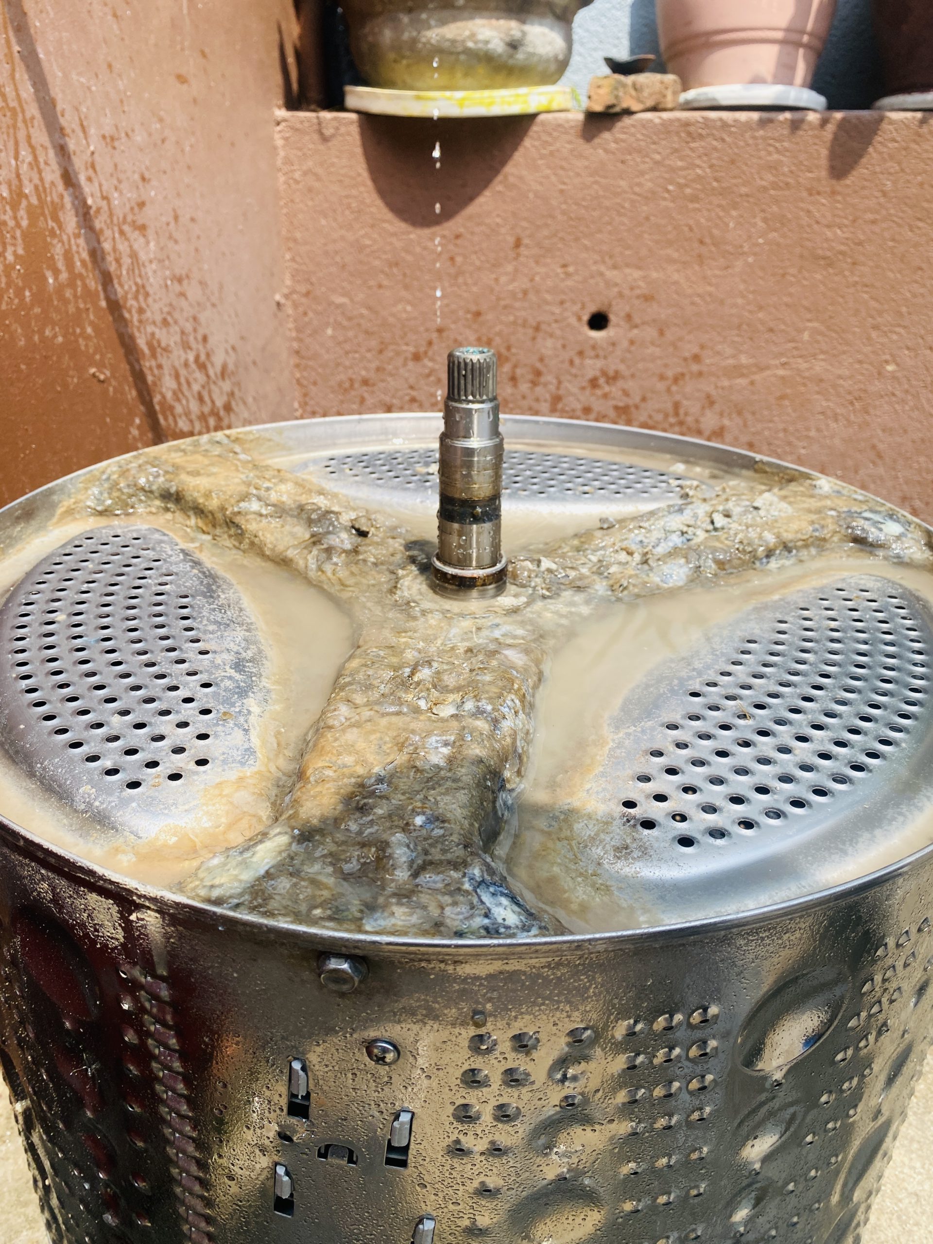 Washing machine inner drum and spider shaft removed, showing heavy limescale and detergent build-up