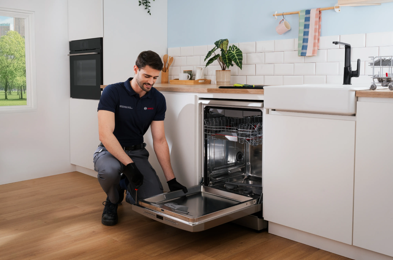 Uniformed appliance repair technician servicing a kitchen appliance at a customer's home